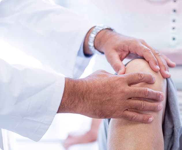 Joelho de um paciente sendo avaliado pelas mãos de um doutor.